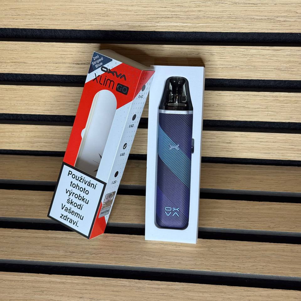 A vape device in its white retail box next to its red and white packaging, placed on a light wood slatted surface.
