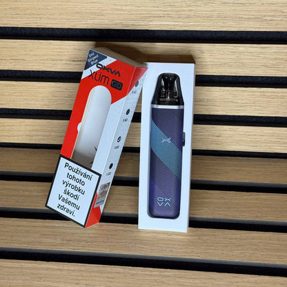 A vape device in its white retail box next to its red and white packaging, placed on a light wood slatted surface.